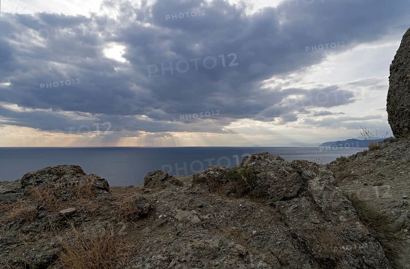 The rays of the sun over the sea make their way through the clouds.Cape Meganom, Crimea, mid-October