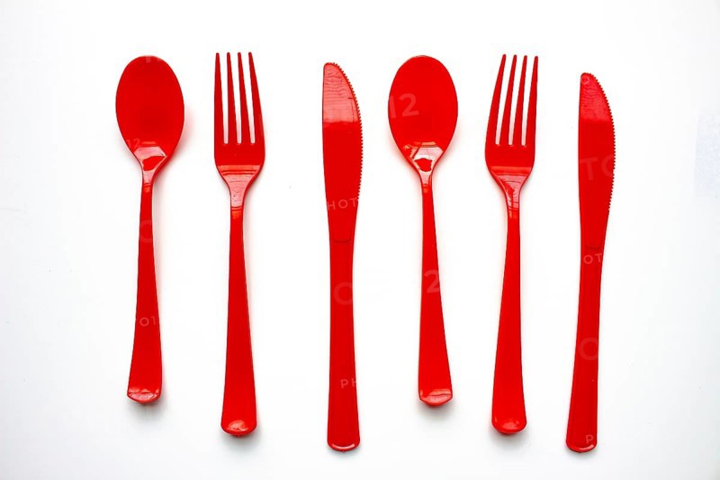 Single use red plastic cutlery on a white background. Concept: Ban single use plastic