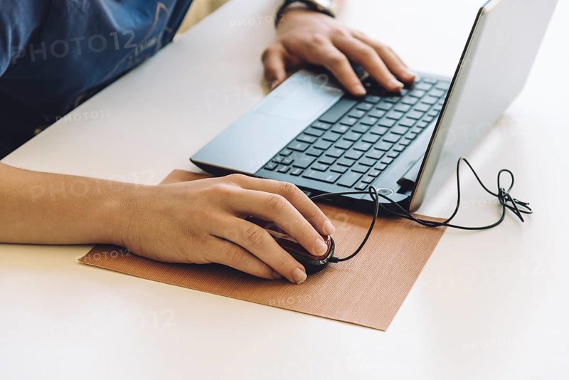 Young man working with laptop, hands on notebook computer and mouse. Blurred background. Student working at home