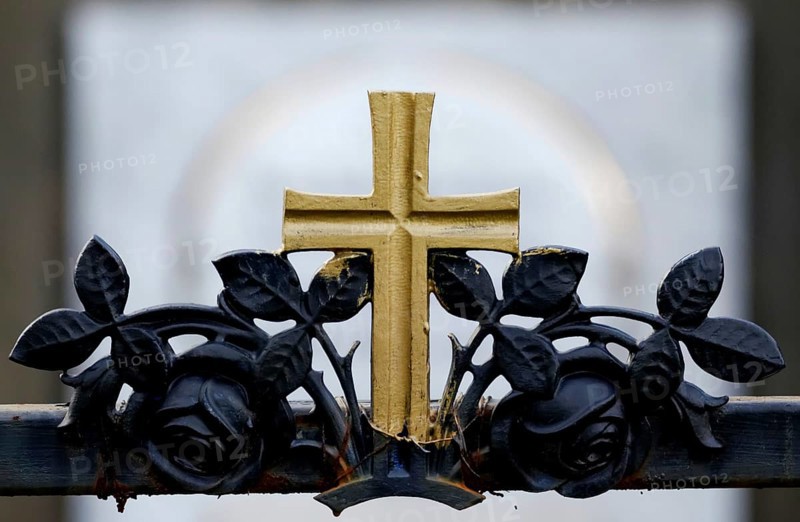 Golden cross on a wrought-iron fence of a grave in a cemetery