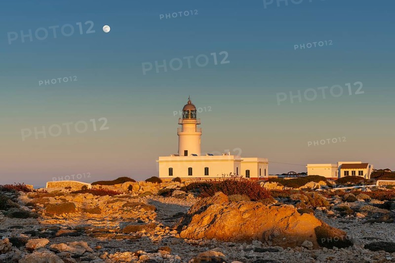 A view of the Cap de Cavalleria Lighthouse on Menorca at sunset with a full moon rising