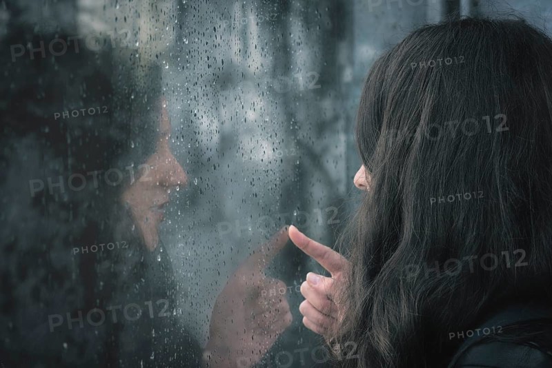 Brunette young woman and her reflection on a window covered with raindrops
