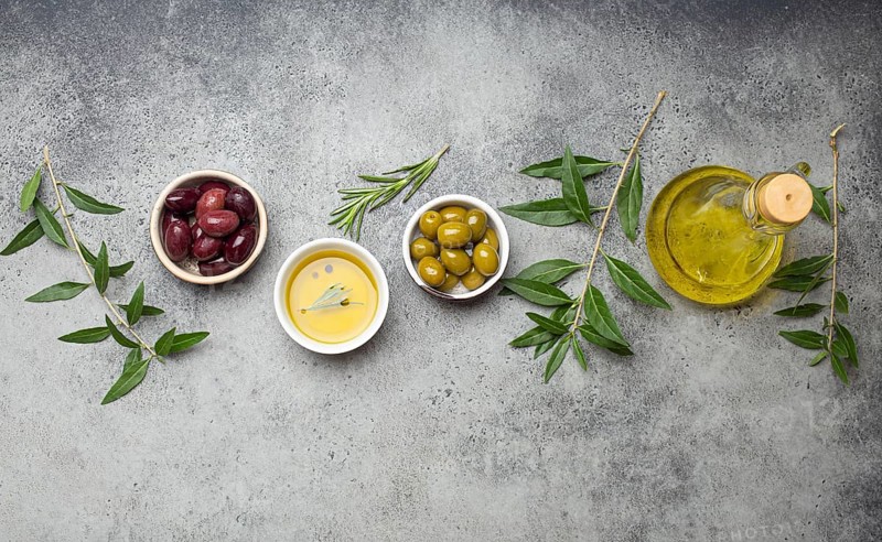 Composition with green and brown olives, extra virgin olive oil in glass bottle, olive tree branches on gray concrete stone rustic background overhead, Mediterranean concept, food photography, food photography