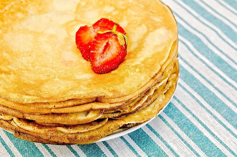 Pancakes stacked on a plate with strawberries on a green striped napkin