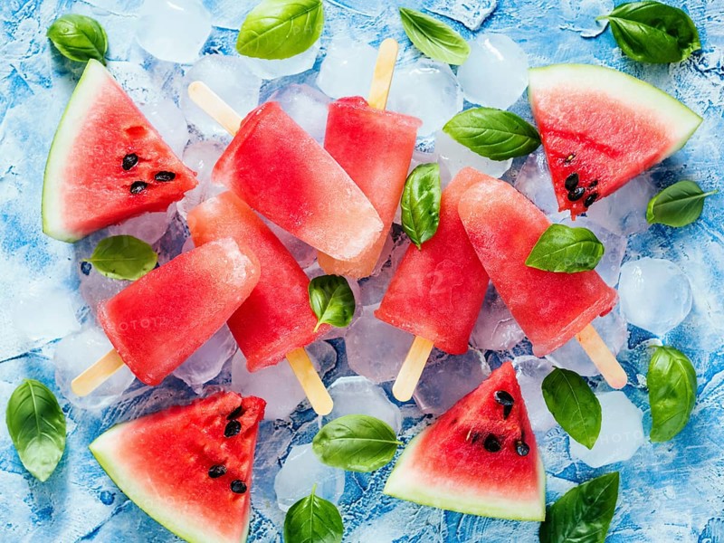 Top view of watermelon and basil popsicles on blue background with fresh green basil leaves and watermelon slices. Popsicles recipe idea