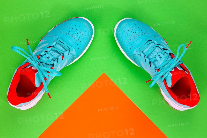 Red, cyan, white pair of new tennis shoes in studio shot over green and orange background. Directly from above