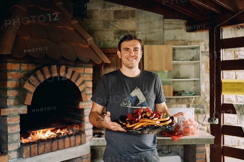 Smiling chef holding big platter with grilled vegetables.