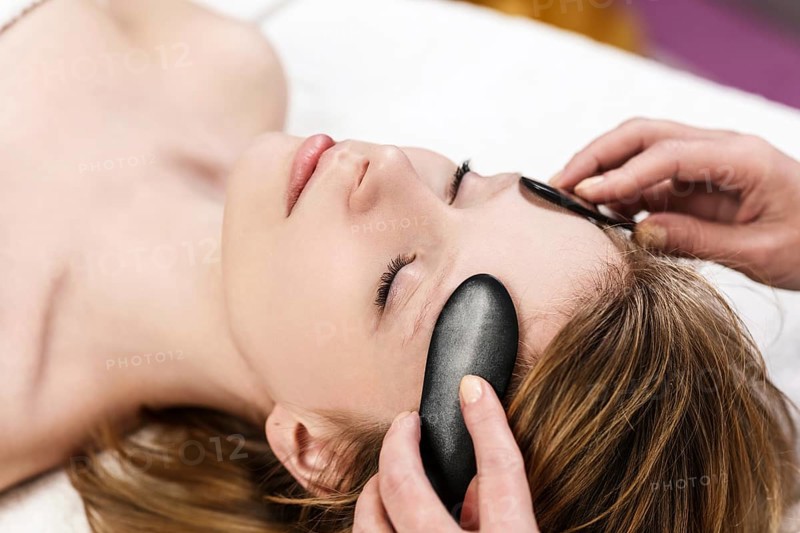 Young woman receiving facial massage with mineral stone