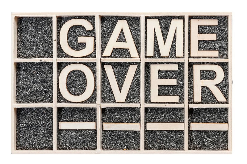 In a collecting box with black decorative sand arranged plywood letters the word GAME OVER stacked in top view on white background