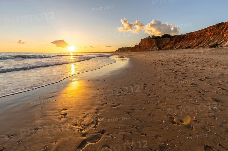 Beautiful sandy beach with red rocks and cliffs. Twilight at sunset with shallow waves on the Atlantic coast in Praia do Poço Velho, Praia da Falésia, Algarve, Portugal, Europe
