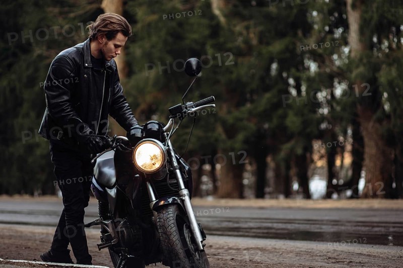 Man in leather jacket with motorcycle on a forest road, evoking a moody, autumn atmosphere
