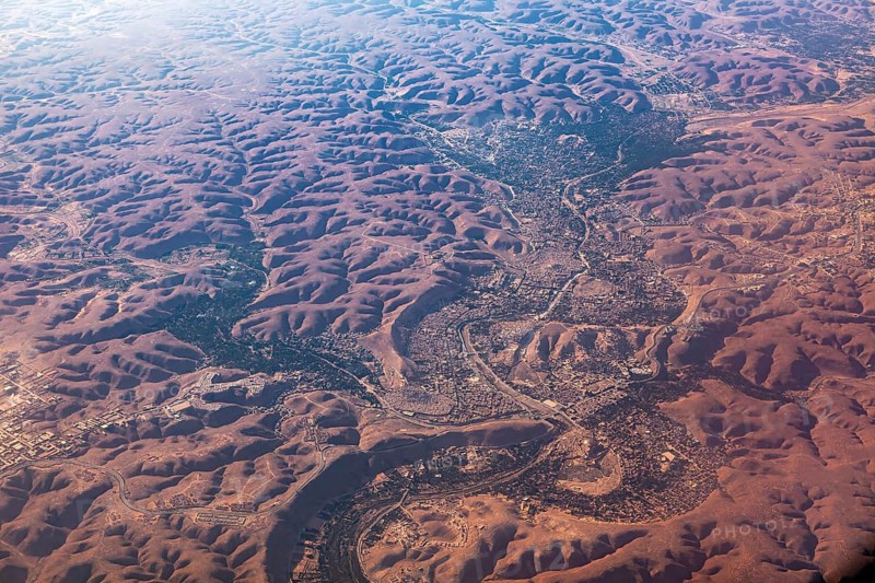 Aerial view of a vast, reddish desert landscape with river valleys and hilly areas, The dunes of the Endless Sahara from the air in Algeria