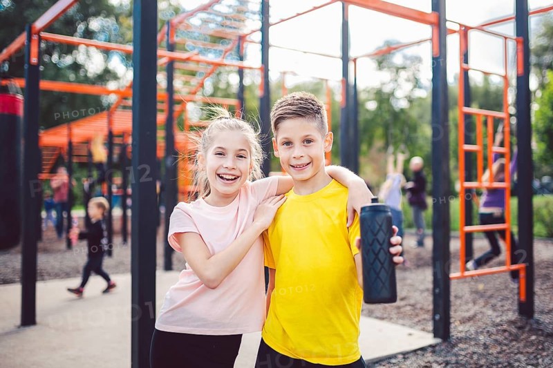 Sportive friends. Brother and sister standing together at street city gym. Children athletes hug smile during workout training. Twins boy and girl posing on playground. Physical development education
