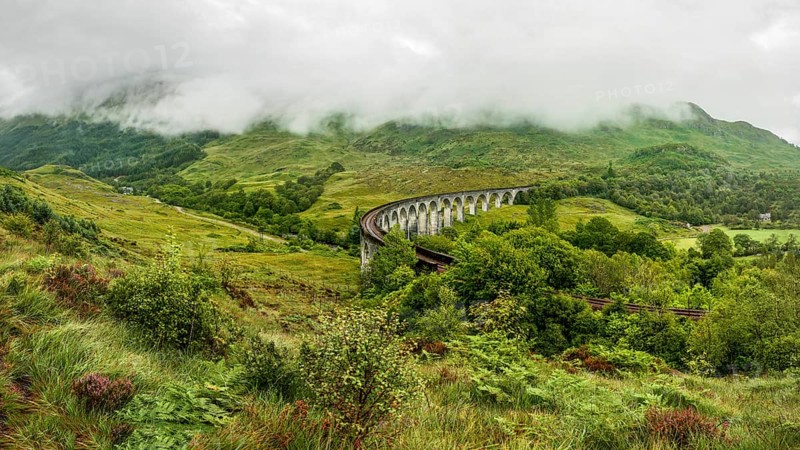 Glenfinnan railway viaduct (location from Harry Potter movie), on overcast day with grey sky and lot of green grass and trees around. Inverness, Scotland, United Kingdom, Europe