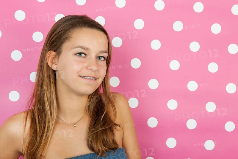 Studio portrait teen girl with long hair on pink background with dots