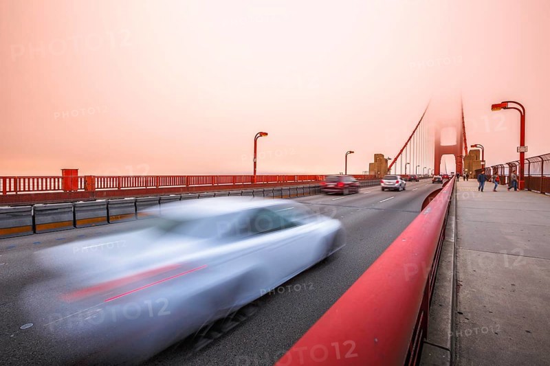 Cars crossing the San Francisco, Californian Golden Gate Bridge from the Presidio Pacific point to the north at sunset light. People along the bridge in the fog. Motion blur effect