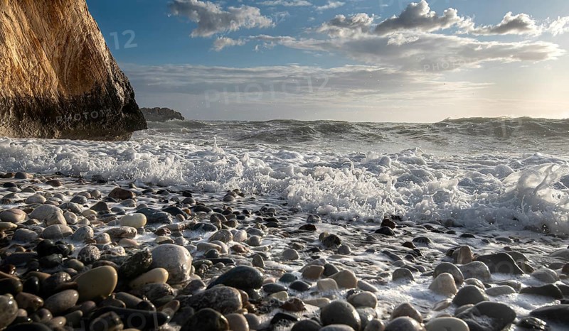 Low angle view of seascape with windy waves splashing on the rock and the sea pebbles. Rock of Aphrodite in Paphos, Cyprus, Europe