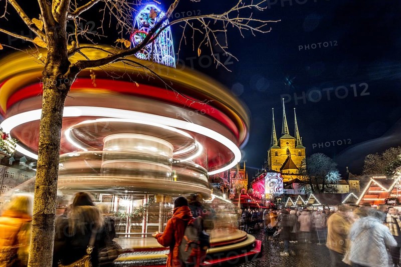 Lebhafte Szene eines Weihnachtsmarktes bei Nacht mit einem Karussell in Bewegung und Kirchtürmen im Hintergrund, Erfurter Weihnachtsmarkt Erfurt
