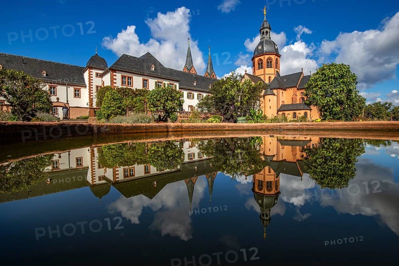 A historic monastery in the morning. Monastery walls, church and buildings are reflected in the water of a fountain. Beautiful garden in Seligenstadt Monastery, Germany, Europe