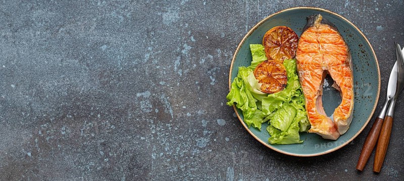 Grilled fish salmon steak and green salad with lemon on ceramic plate on rustic blue stone background top view, balanced diet or healthy nutrition meal with salmon and veggies, food photography, food photography