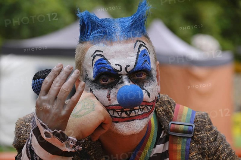 A clown with a microphone and striking make-up, menacing atmosphere outdoors