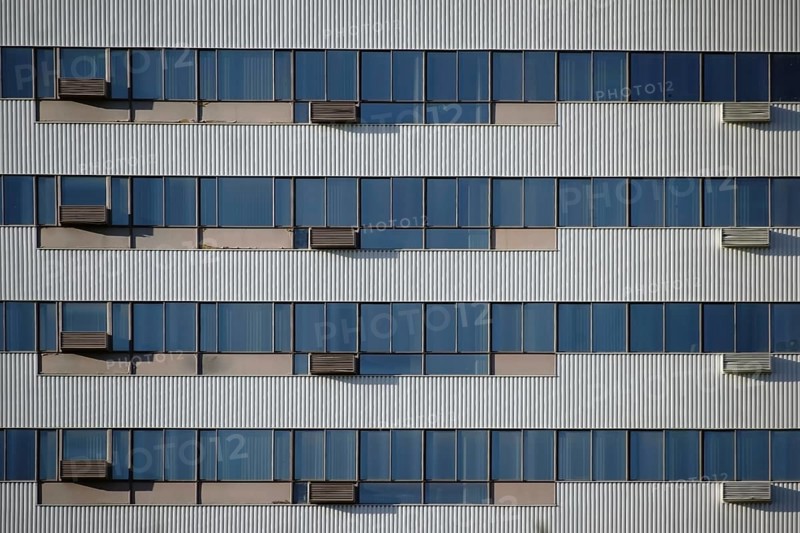 The modern façade and exterior wall of an office building with solar control windows and air conditioning systems