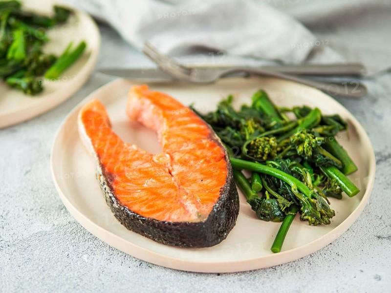 Ready-to-eat grilled salmon steak and greens - baby broccoli or broccolini and spinach on rustic craft plate over gray background. Keto diet dish