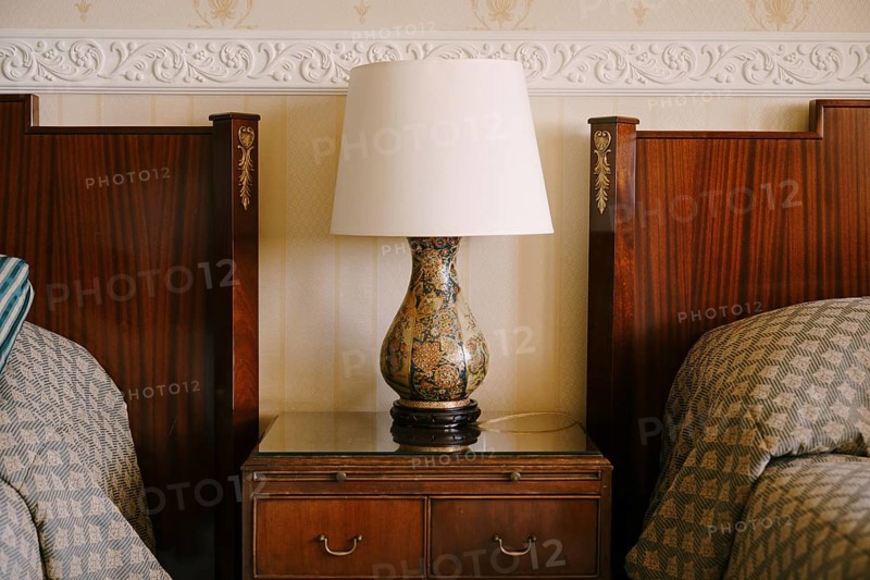 Bedside lamp on the nightstand. Refined and rich interior. Wooden bedside table next to two beds.