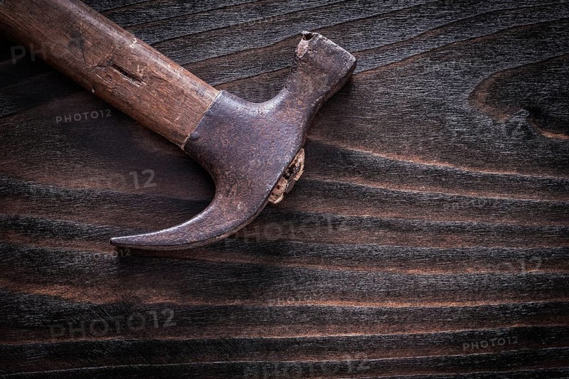 Rusty metal claw hammer on vintage dark wooden board top view construction concept