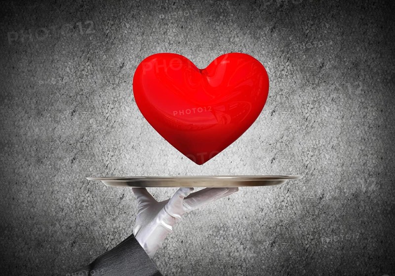 Cropped image of waitress's hand in white glove presenting big red heart on metal tray with dark wall on background