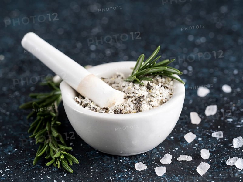 Close up view of mortar and pestle with sea salt scented rosemary and lemon zest. Sea salt scented herb rosemary on dark blue background. Scented salt and ingerdients. Copy space