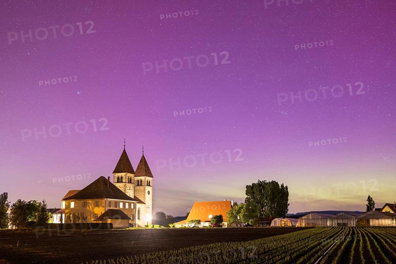 Church of St Peter and St Paul under a purple starry sky with aurora borealis, surrounded by fields at dusk, Reichenau, Lake Constance, Baden-Württemberg, Germany, Europe
