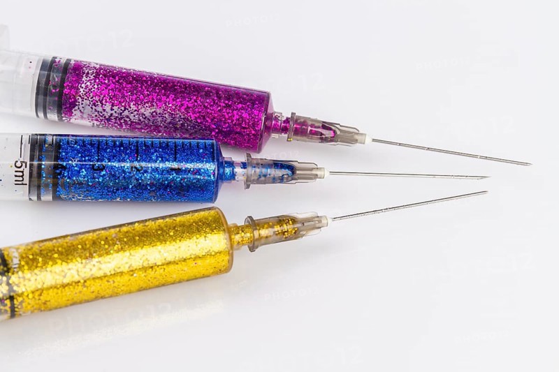 Close up of syringes with colorful glitter. Isolated on white