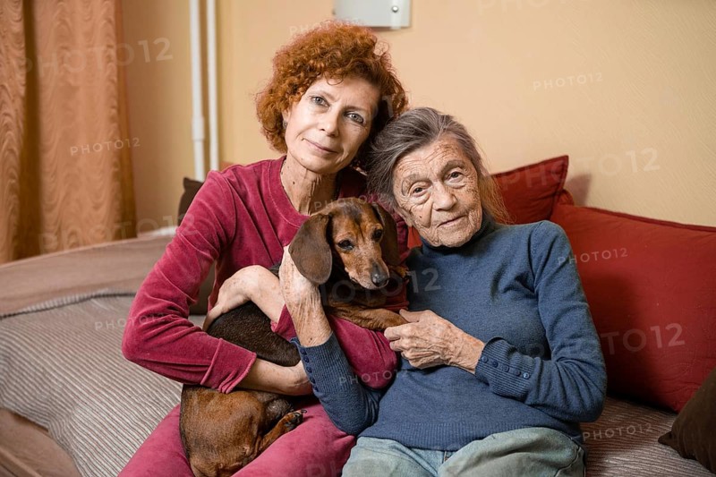 The theme is animal therapy, caring for elderly with dementia and Alzheimer's disease. Adult women spend time with elderly mother and pets dogs to bring joy and pleasure, affection for loved ones