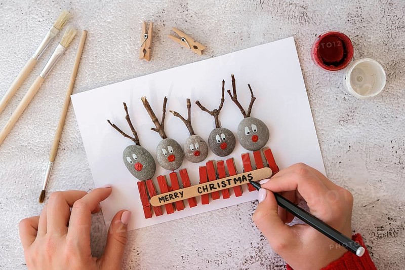 Diy Merry Christmas deer on greeting card postcard made of pebbles, sea stones, clothespins and branches on white background. Natural Eco style diy. Gift idea. Step by step. Top view. Process kid children craft. Do it yourself