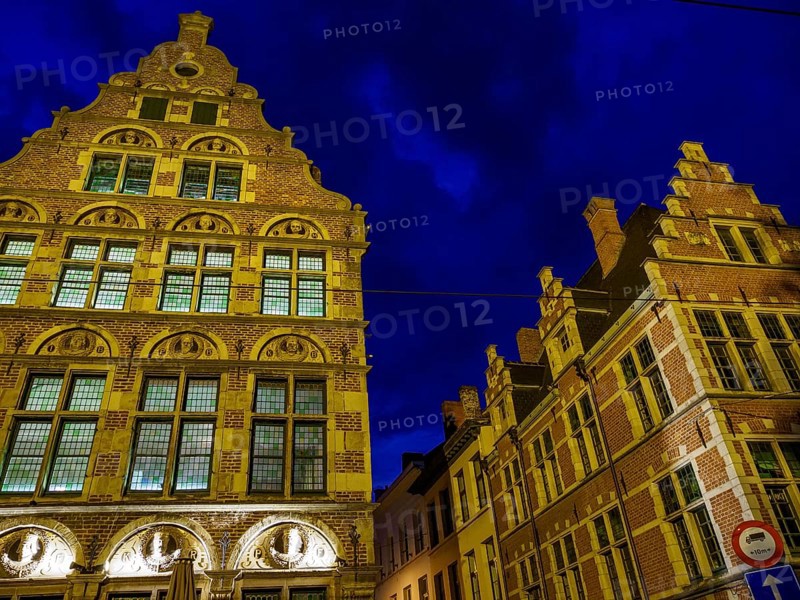 Two illuminated historical buildings at night, glowing in blue light. Cloudy sky, Ghent, Belgium, Europe