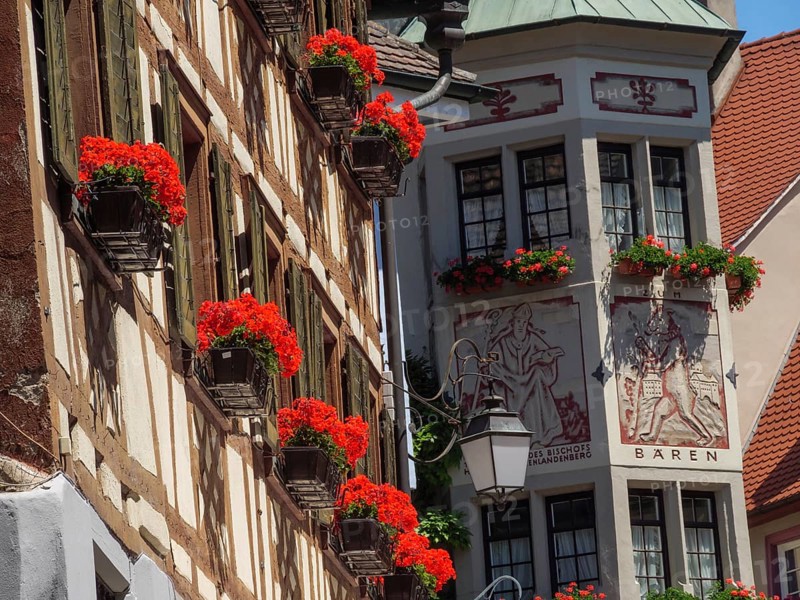 Historic half-timbered house with windows and red flowers under a blue sky, Meersburg, Lake Constance, Germany, Europe