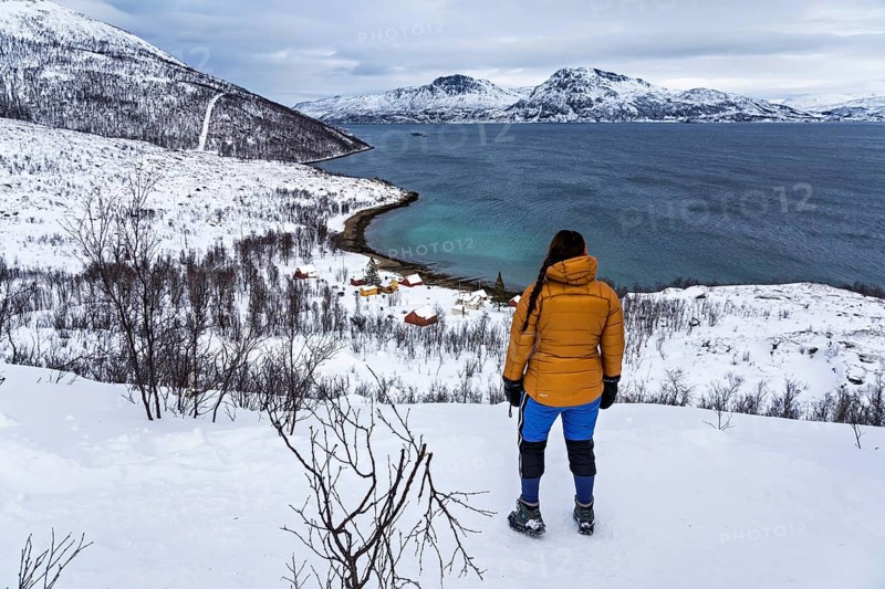 A woman in winter clothing stands above the small bay of Skjellvika on the island of Kvaloya, Tromso, Troms, Norway, Europe