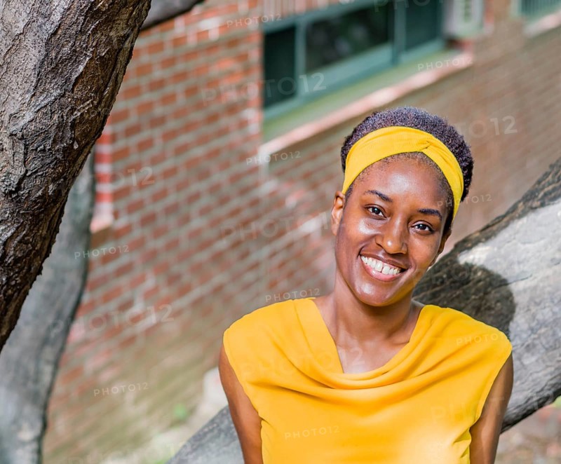 Smiling woman in a yellow dress with a headband, standing near a tree and brick wall, Taken in Daejeon, South Korea, Asia