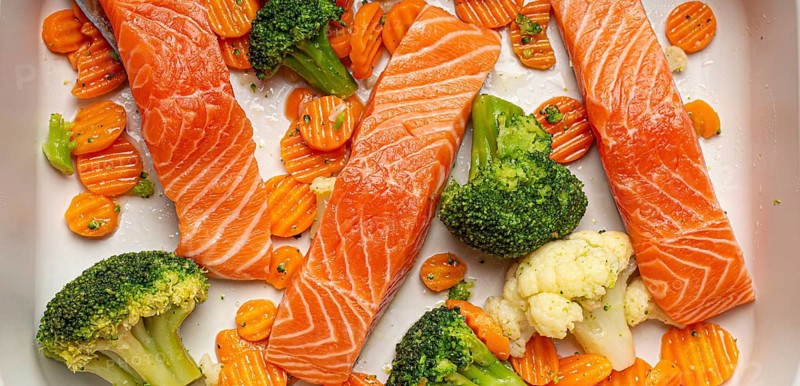 Top view of baking dish casserole with raw uncooked fish salmon steaks, broccoli, cauliflower, carrot. Preparing a healthy low carb dinner concept, food photography
