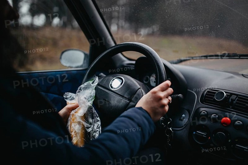 Person holding a sandwich and steering wheel in a car, capturing a casual driving moment