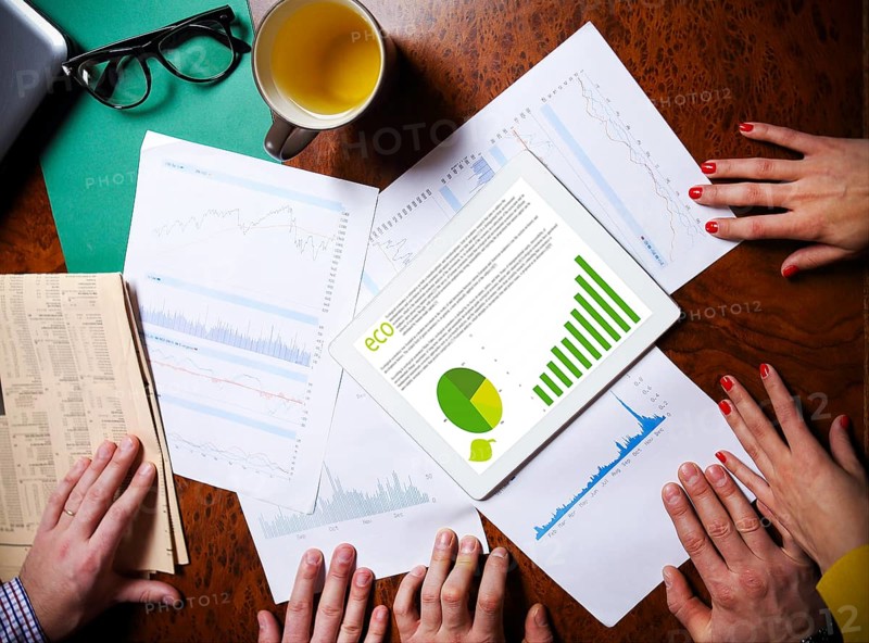 Business team hands at work with financial reports and a tablet computer, top view