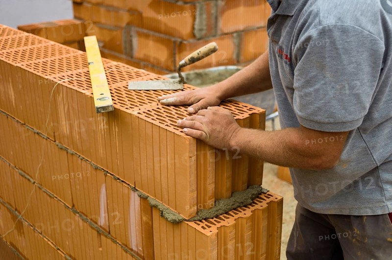 Anonymous construction worker on a building site erecting a brick wall. Brick wall of a solid house. Symbolic image for illegal labour and bungling