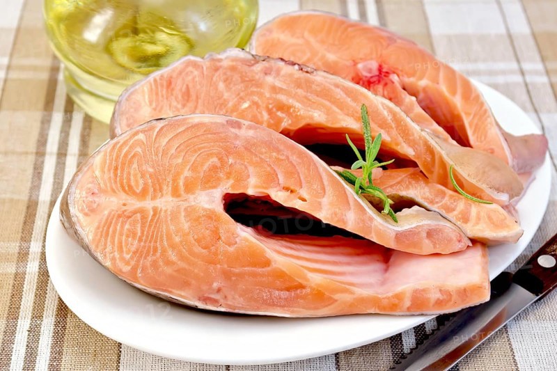 Three pieces of trout in white plate with rosemary oil in a glass decanter on a background of checkered fabric