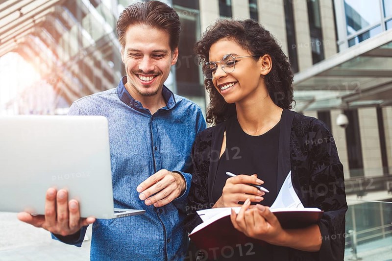 Two smiling colleagues are chatting in the street during lunch break near the building in the background