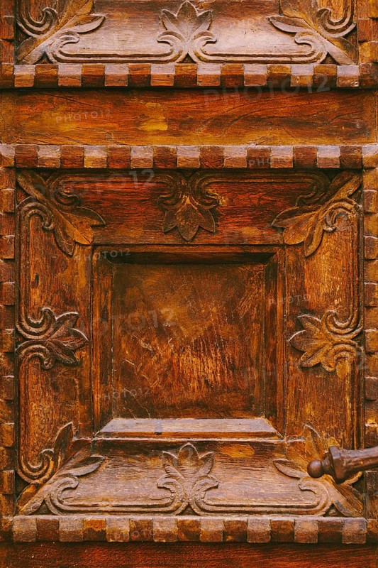Close-up texture of brown wooden doors with raised carvings and square patterns.