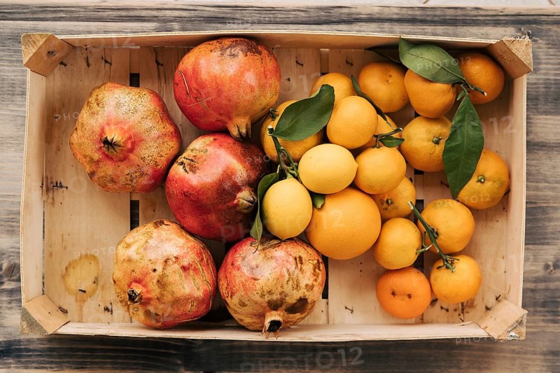 A wooden box with tangerines, lemons and pomegranates. Fruits collected in the autumn garden.