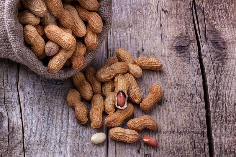 Peanuts in a burlap sack on wooden background