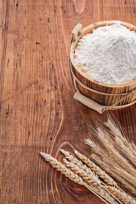 Flour in wooden bucket with ears of wheat on old table