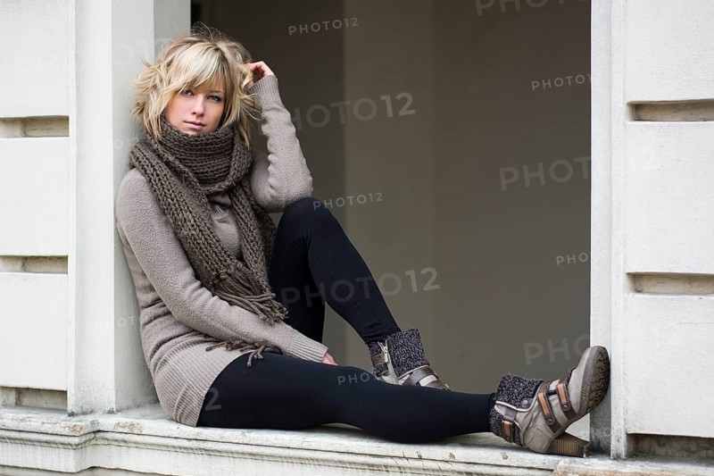 Attractive blonde young woman sitting on window sill, wearing winter clothes